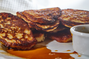 Pancakes on white plate and sweet liquid honey or caramel with a small spoon and with background. Delicious fried flour food. Unhealthy and harmful, but very tasty food.