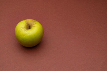 Green apple on a brown background. Minimalistic composition. Background for text or design