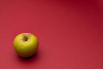 Green apple on a red background. Minimalistic composition. Background for text or design