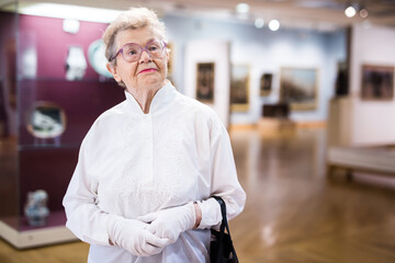Fototapeta premium mature woman examines paintings in an exhibition in hall of an art museum