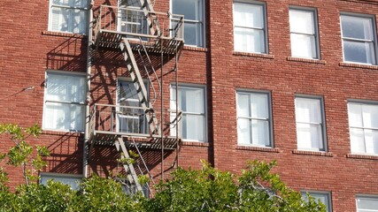 Fototapeta na wymiar Fire escape ladder outside residential brick building in San Diego city, USA. Typical New York style emergency exit for safe evacuation. Classic retro house exterior as symbol of real estate property