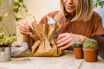 Young smiling woman uniting twine from paper bag near cactuses and expanded clay on table  