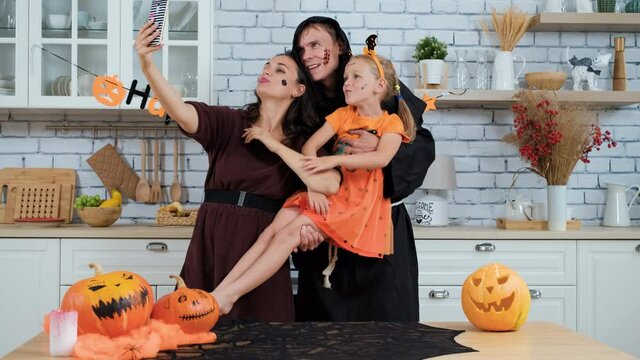 Funny Family in Costumes and Makeup Taking Photos on Smartphone on Halloween Party. Father, Mother and Little Daughter Having Fun in the Kitchen. People and Halloween Holiday Concept