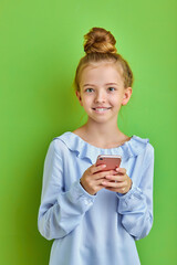pretty caucasian kid girl using smartphone, chatting with friends, typing. isolated on green background, studio shoot
