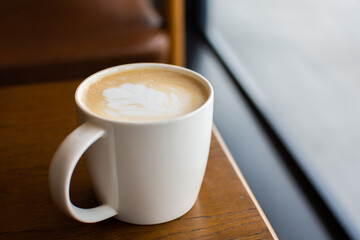 White coffee cup with foam latte art on a brown wooden table in the coffee shop