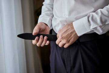 Naklejka premium Businessman putting on a belt, fashion and clothing concept,groom getting ready in the morning before ceremony