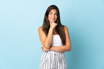 Young brazilian woman isolated on blue background thinking an idea while looking up