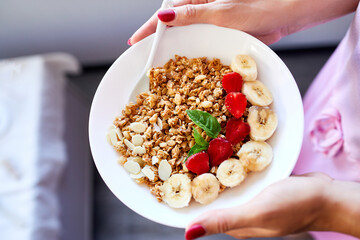 Woman eating healthy breakfast bowl, hold in hand granola, seeds, fresh strawberry, banana, top view, copy space. Clean eating, detox, dieting, vegetarian food concept