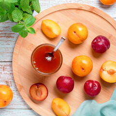 Yellow and red plums in a plate and jar of plum jam on worn wooden table flat lay, autumn fruit preserves concept, copy space