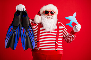 Photo of grandfather grey beard hold paper plane diving gear flippers wear santa claus x-mas costume suspenders sunglass striped shirt cap isolated red color background