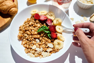 Woman eating healthy breakfast bowl, hold in hand granola, seeds, fresh strawberry, banana, top view, copy space. Clean eating, detox, dieting, vegetarian food concept