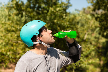 a roller skater with a helmet and is drinking water, he wears a covid protection mask on his arm. © Jordi Mora