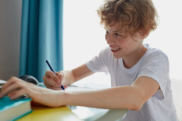 happy child boy doing homework, caucasian curly boy writing on notebook, looks away