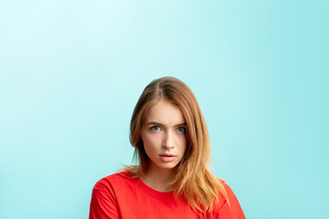 Fototapeta premium Shocked woman portrait. Special offer. Overwhelmed lady in red with nude makeup looking at camera isolated on blue copy space advertising background. Wtf reaction. Unexpected news.