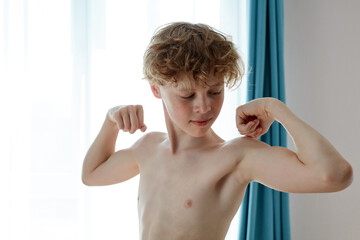 young caucasian teenager boy showing arms muscles, proud. fitness concept. at home