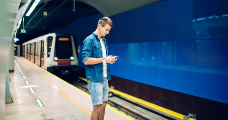 Fototapeta premium Stylish man with smartphone waiting for train