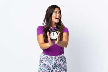 Young brazilian girl isolated on white background in pajamas and holding clock