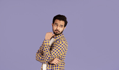 Thoughtful Indian guy looking over his shoulder at empty space, lilac background