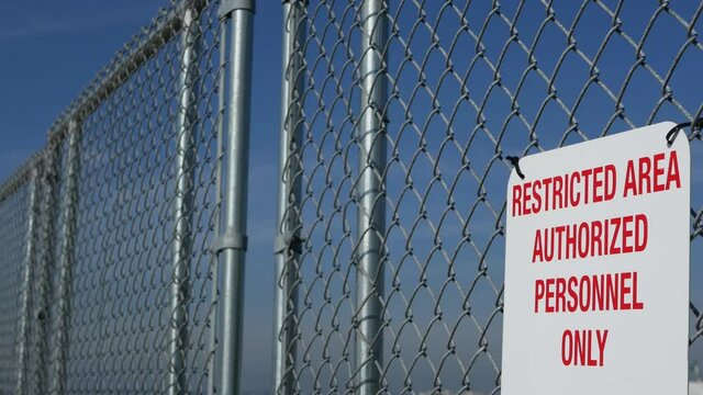 Restricted area, authorized personnel only sign in USA. Red letters, keep off warning on metal fence, United States border symbol. No trespassing notice means violators will be prosecuted by US law.