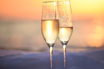 Two glasses of champagne close-up against the background of the sea at sunrise.