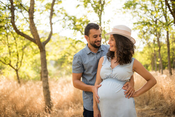 Fototapeta premium Couple waiting for a baby posing in the trees with sunset light.
