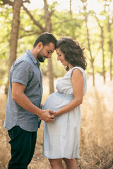 Obraz premium Couple waiting for a baby posing in the trees with sunset light.