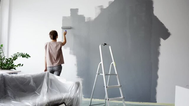 Footage with young woman painting wall at home using roller brush