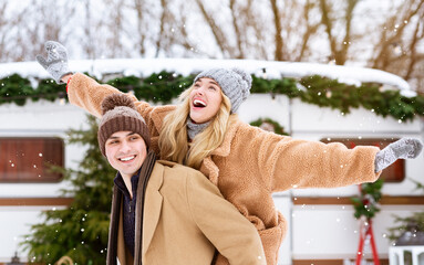 Happy winter couple having fun outdoors at campsite, guy piggybacking his girlfriend