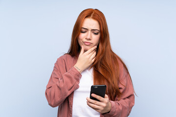Redhead teenager girl over isolated blue background thinking and sending a message