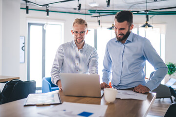 Smiling caucasian male entrepreneurs having positive conversation watching video on laptop computer...