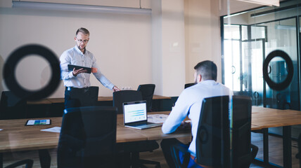 Confident male entrepreneurs cooperating on common project communicating using digital devices, caucasian 20s men colleagues in smart casual clothes analyzing information about project at consultancy