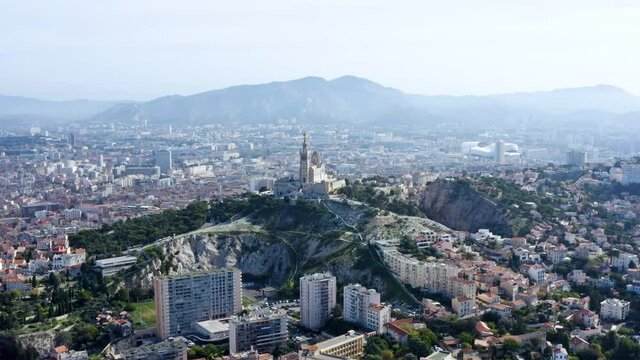 Panoramic aerial view of Notre-Dame de la Garde church and Marseille cityscape. Grand basilica the bell tower landmark at the city's highest point, crowned by golden statue of Mary in France 4K