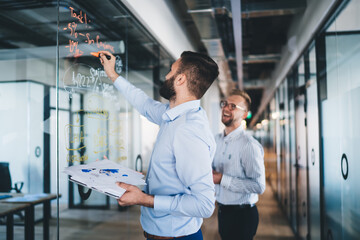 Confident man spending time for training business person writing information on modern board during cooperation with partner discussing ideas for startup project, accounting briefing in office