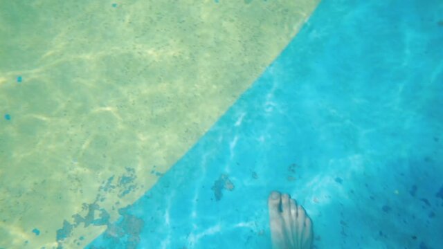 CZ, Pecka, 25.6.2020. Feet walk on the blue-yellow bottom of the pool at a closed water park. First-person view. Search for valuables lost jewellery and keys while swimming. 