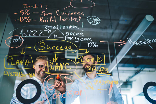 Smiling young experts looking at sketches and infographics enjoying productive cooperation on working process, positive male employee showing information to boss on consultancy explaining opinion