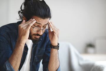 Young indian guy freelancer suffering from headache after hard working day - obrazy, fototapety, plakaty