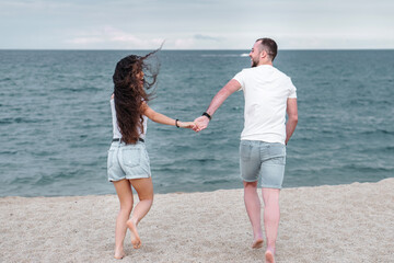 Young couple running on the beach holding hands and enjoying and having fun  in matching outfits....