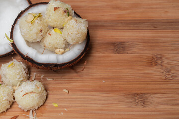 Candies in coconut flakes and fresh coconut on light wooden background with space for text