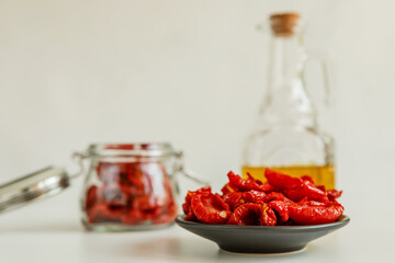 Homemade sun-Dried tomatoes on a black saucer, olive oil in a glass bottle on a light background. Print for the kitchen. selective focus.