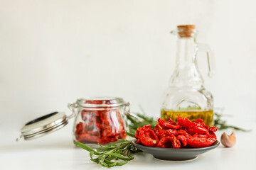 Homemade sun-Dried tomatoes, olive oil in a glass bottle, fresh rosemary and spices on a light background. Print for the kitchen. selective focus.