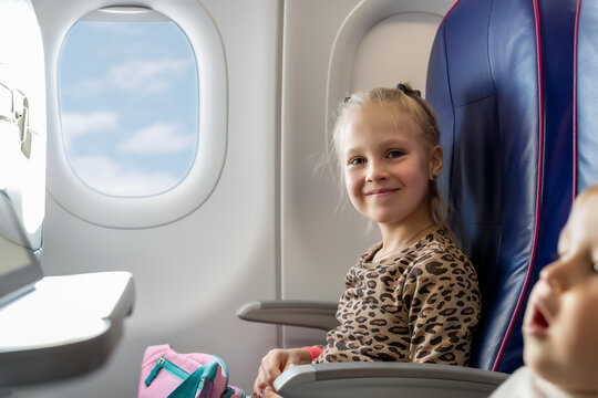 Pair of cute little adorable sibling brother and sister traveling by plane. Boy and girl sit inside aircraft during flight. Children watching cartoons by table. Happy family trip concept