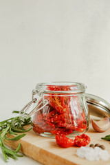 Homemade sun-dried tomatoes in a glass jar, fresh rosemary, on a light background. place to copy. selective focus.