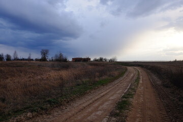 A bend in a country road in an evening field. Twilight landscape. Dramatic cloudy sky.