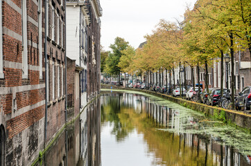 Delft, The Netherlands, September 8, 2020: Old Delft canal on a day in autumn with waterside buildings on one side and a tree-lined quay on the other isde