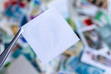 Blank square postage stamp against blurred background collection of multicolored postage stamps of different countries. Selective focus