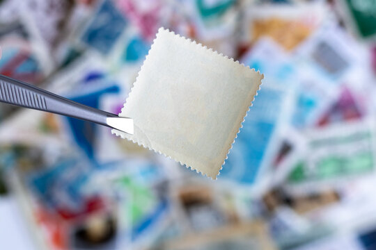 Blank Square Postage Stamp Against Blurred Background Collection Of Multicolored Postage Stamps Of Different Countries. Selective Focus