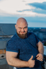 Big bearded bodybuilder on the rooftop in the evening.