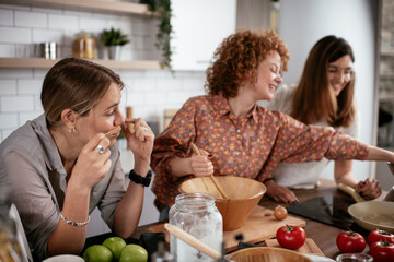 Girlfriends having fun in kitchen. Young girls preparing delicious food at home.
