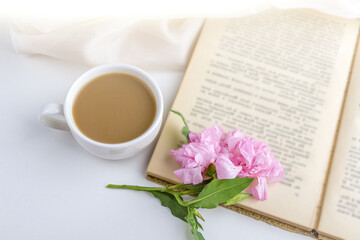 Romantic vintage still life with pink flowers, old book, cup of tea or coffee in spring, summer day in garden. Coffee time