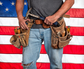 Male carpenter holding hammer, wearing old, leather tool belt with hand tools, American flag, usa,...